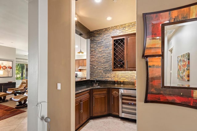 bar with dark stone counters, sink, light tile patterned floors, decorative light fixtures, and beverage cooler