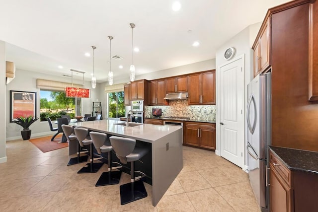 kitchen featuring pendant lighting, a center island with sink, light tile patterned floors, a kitchen bar, and stainless steel appliances