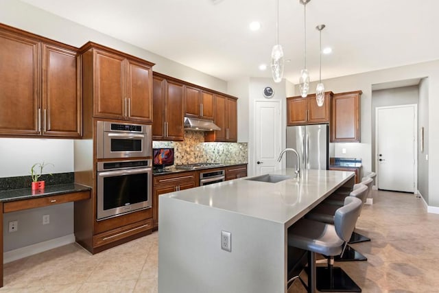 kitchen with sink, stainless steel appliances, a kitchen breakfast bar, pendant lighting, and a kitchen island with sink