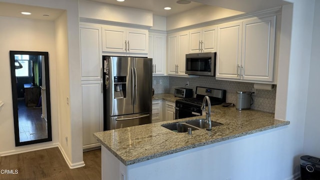 kitchen with kitchen peninsula, appliances with stainless steel finishes, light stone counters, dark hardwood / wood-style floors, and white cabinetry