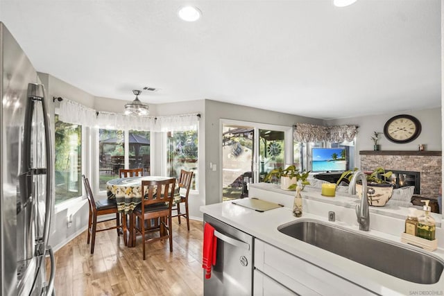 kitchen featuring appliances with stainless steel finishes, sink, light hardwood / wood-style flooring, white cabinets, and a stone fireplace