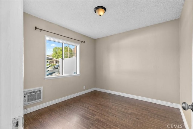 empty room featuring a textured ceiling, a wall unit AC, and dark wood-type flooring