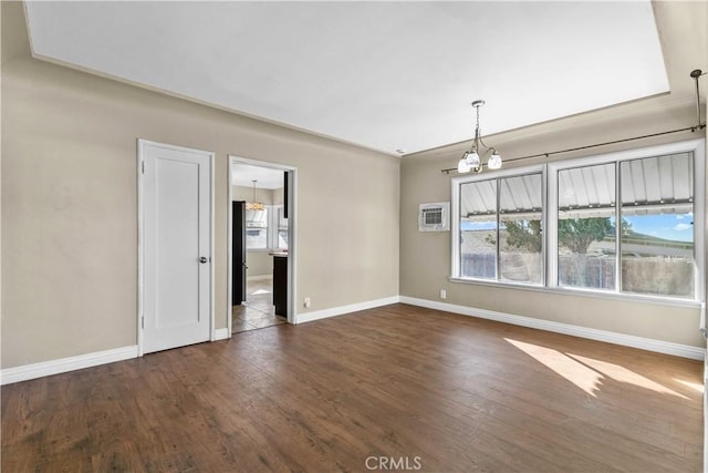 empty room with dark hardwood / wood-style floors, a wall unit AC, and an inviting chandelier