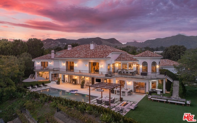 back house at dusk with a mountain view, a patio, and a balcony