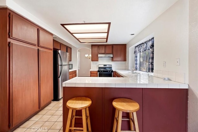 kitchen with stainless steel appliances, kitchen peninsula, tile countertops, light tile patterned flooring, and a breakfast bar