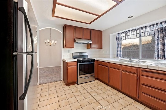 kitchen with appliances with stainless steel finishes, tile counters, light carpet, sink, and a chandelier