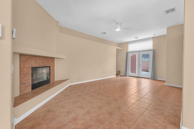 unfurnished living room featuring ceiling fan, a fireplace, light tile patterned floors, and french doors