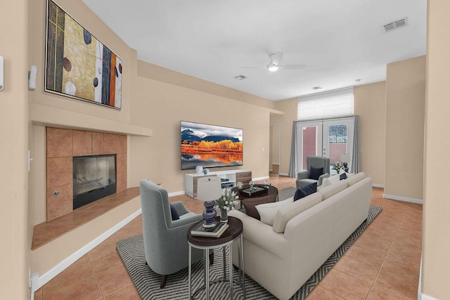 living room featuring a tile fireplace, light tile patterned floors, french doors, and ceiling fan