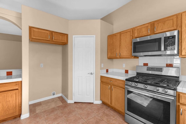 kitchen featuring tile countertops, decorative backsplash, light tile patterned floors, and stainless steel appliances