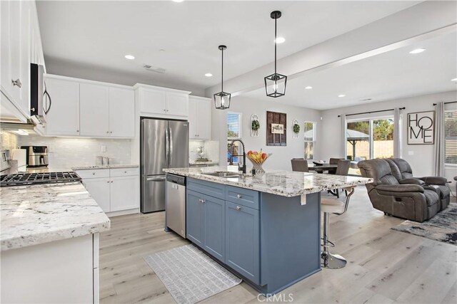 kitchen with a kitchen island with sink, white cabinets, sink, hanging light fixtures, and stainless steel appliances