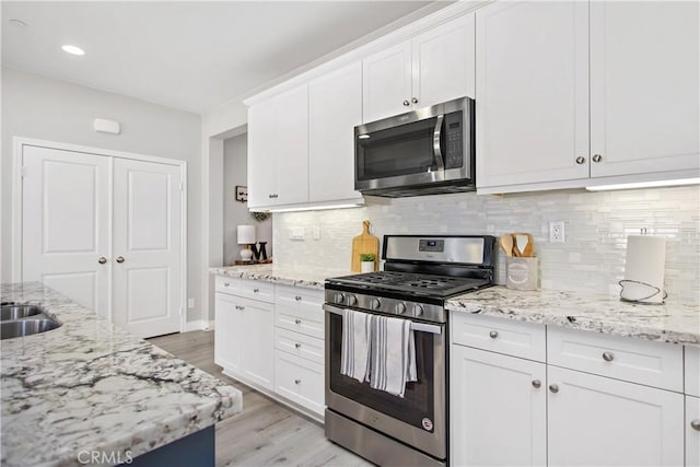 kitchen featuring white cabinets, light stone countertops, backsplash, and appliances with stainless steel finishes