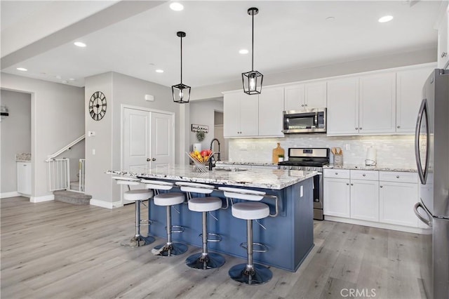 kitchen featuring stainless steel appliances, sink, pendant lighting, white cabinetry, and an island with sink