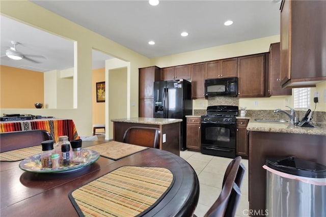 kitchen featuring light stone countertops, sink, ceiling fan, a kitchen island, and black appliances