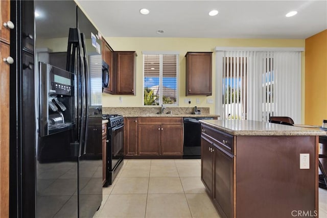 kitchen with black appliances, a center island, light stone countertops, and light tile patterned floors