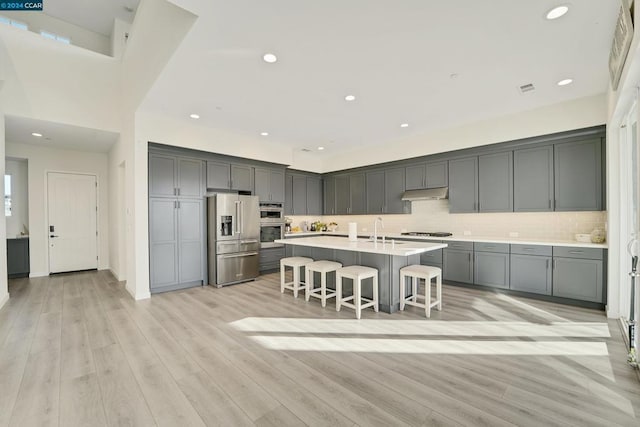 kitchen featuring light wood-type flooring, a kitchen island with sink, appliances with stainless steel finishes, and a breakfast bar area