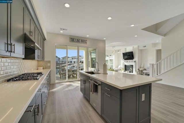 kitchen with gray cabinetry, sink, light wood-type flooring, and an island with sink