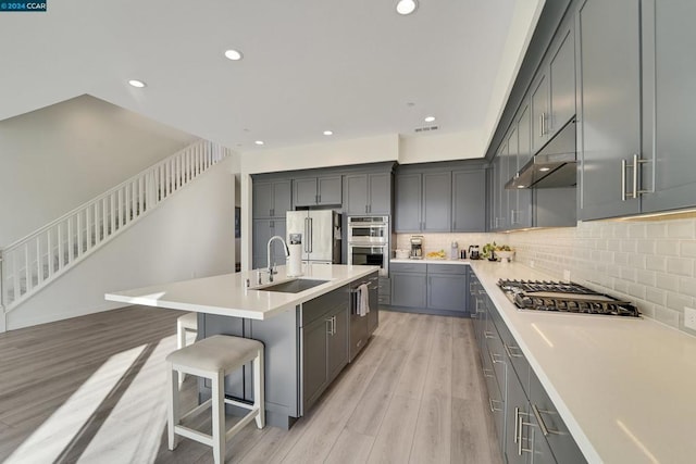 kitchen featuring sink, stainless steel appliances, an island with sink, a kitchen bar, and light wood-type flooring