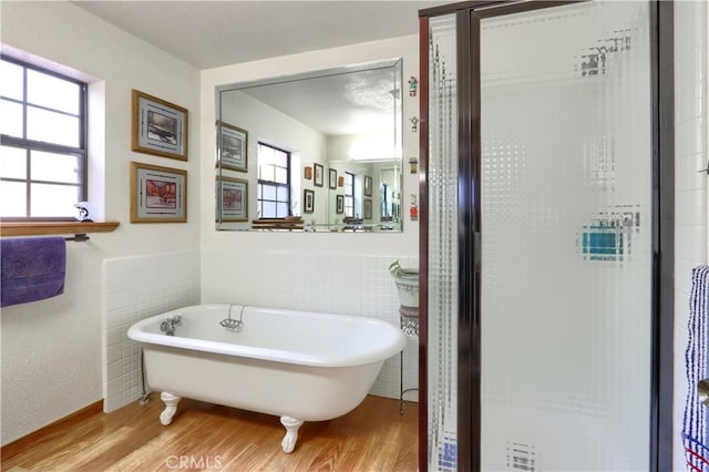 bathroom with hardwood / wood-style floors, a tub to relax in, and tile walls