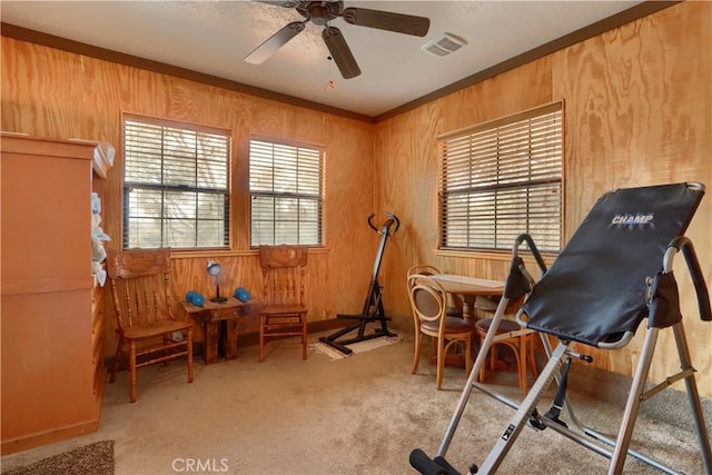 exercise area with ceiling fan, wooden walls, light colored carpet, and ornamental molding