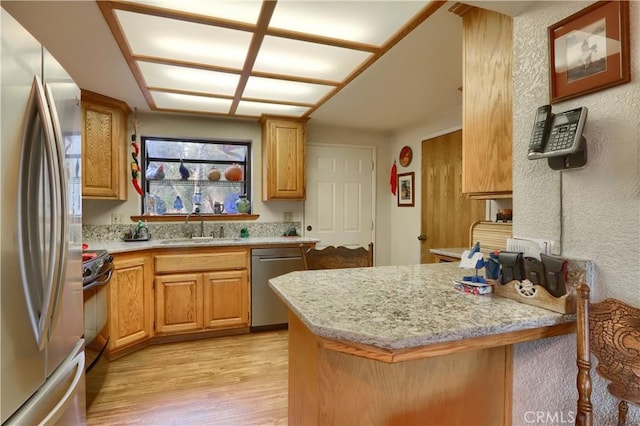 kitchen with sink, light wood-type flooring, a kitchen bar, kitchen peninsula, and stainless steel appliances