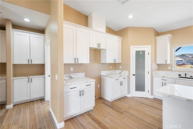 kitchen with white cabinets, light stone counters, and light hardwood / wood-style flooring