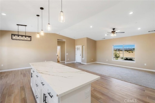 kitchen with light stone counters, vaulted ceiling, ceiling fan, decorative light fixtures, and white cabinets