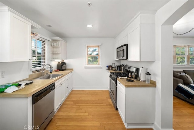 kitchen with a sink, white cabinets, light wood-style floors, appliances with stainless steel finishes, and a wealth of natural light