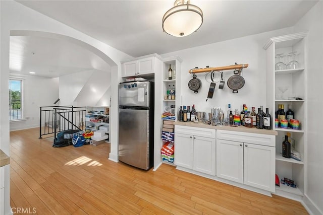 kitchen featuring arched walkways, light wood finished floors, open shelves, freestanding refrigerator, and white cabinets