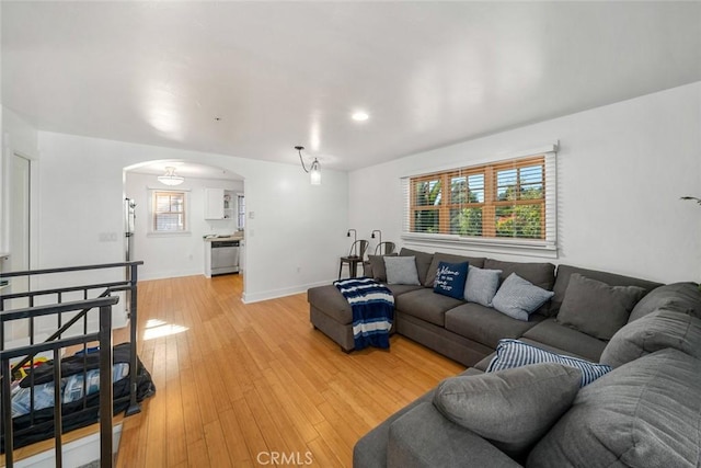 living room featuring arched walkways, light wood-style flooring, and baseboards