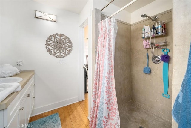 full bathroom featuring tiled shower, vanity, baseboards, and wood finished floors