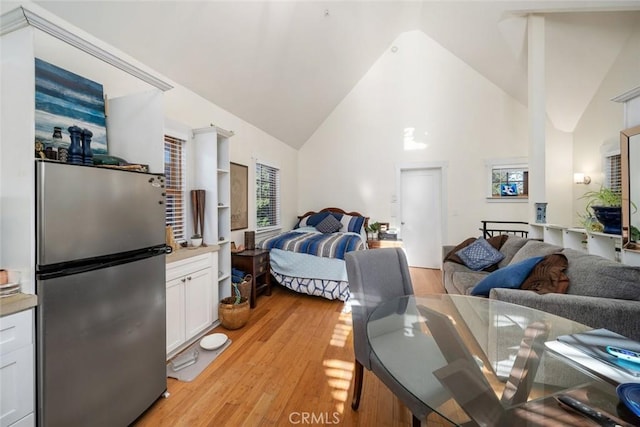 bedroom featuring stainless steel fridge, light hardwood / wood-style floors, and high vaulted ceiling