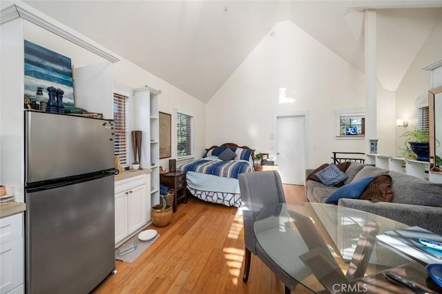 bedroom featuring high vaulted ceiling, light wood-type flooring, and freestanding refrigerator