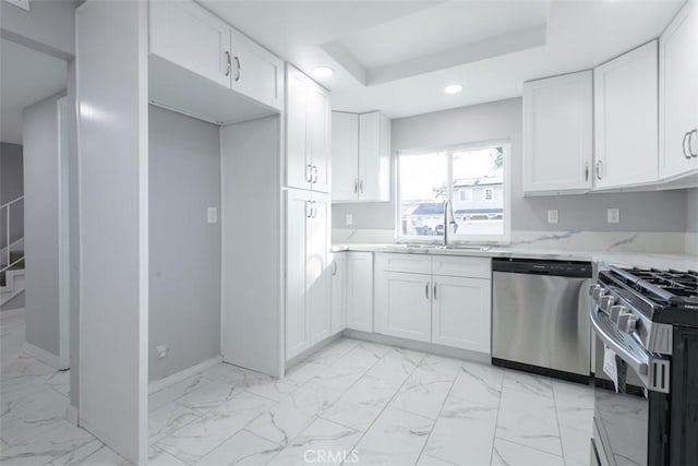 kitchen with sink, stainless steel appliances, a raised ceiling, light stone counters, and white cabinets