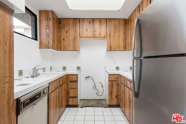 kitchen with sink, tile counters, light tile patterned floors, and appliances with stainless steel finishes