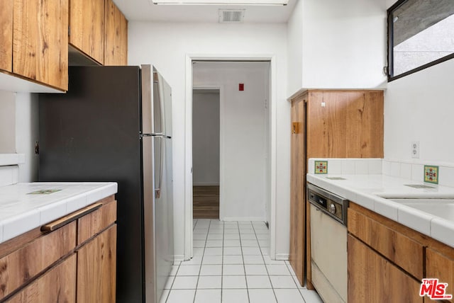 kitchen featuring dishwasher, tile counters, sink, stainless steel fridge, and light tile patterned floors