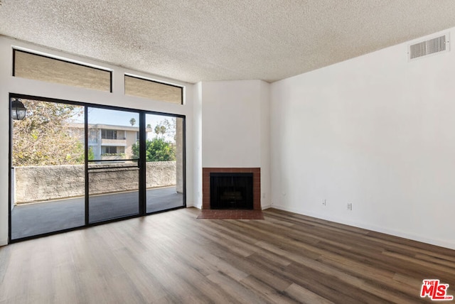 unfurnished living room with wood-type flooring, a textured ceiling, and a brick fireplace