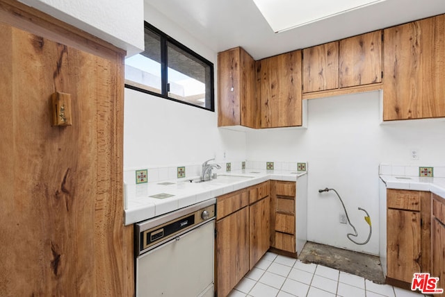 kitchen featuring tile counters, sink, white dishwasher, and light tile patterned flooring