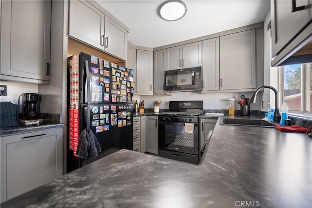 kitchen featuring dark countertops, gray cabinetry, a sink, and black appliances