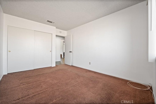 unfurnished bedroom featuring a textured ceiling, a closet, carpet flooring, and visible vents