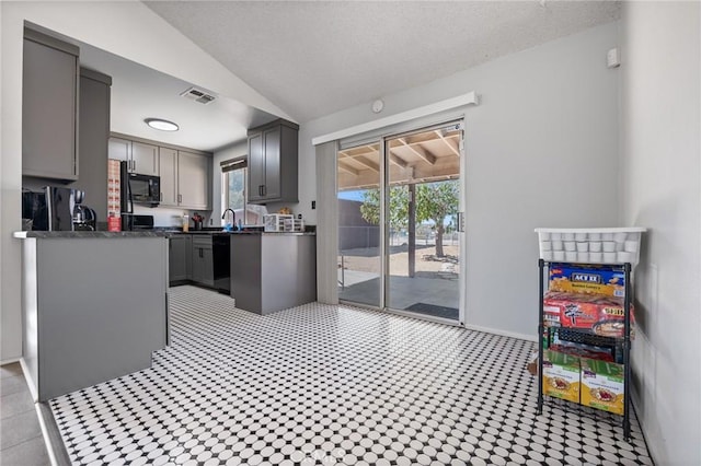 kitchen with visible vents, dark countertops, vaulted ceiling, gray cabinets, and black appliances