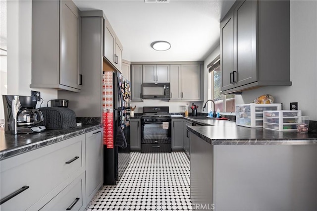 kitchen with dark countertops, light floors, gray cabinets, black appliances, and a sink