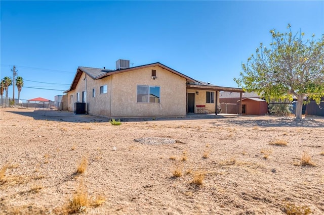 rear view of property with central AC, a shed, fence, and stucco siding