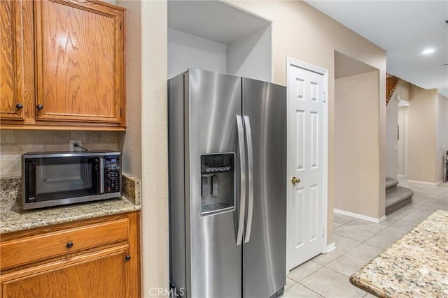 kitchen with stainless steel appliances, light stone counters, and light tile patterned flooring