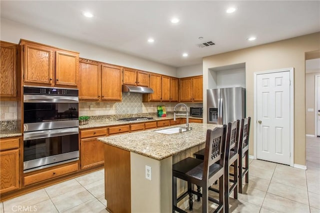 kitchen featuring a breakfast bar, a kitchen island with sink, sink, light stone countertops, and appliances with stainless steel finishes