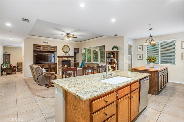 kitchen with dishwasher, sink, hanging light fixtures, a fireplace, and an island with sink