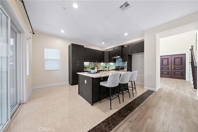 kitchen with a kitchen breakfast bar, tasteful backsplash, light hardwood / wood-style flooring, a kitchen island with sink, and stainless steel stove