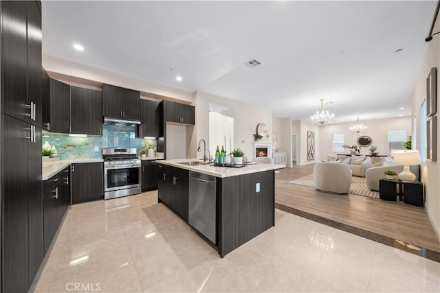 kitchen with sink, decorative backsplash, an island with sink, stainless steel appliances, and a chandelier