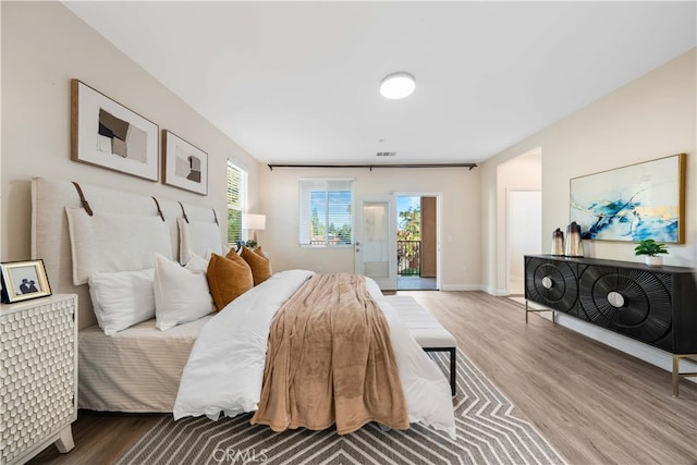 bedroom with access to exterior, wood-type flooring, and multiple windows