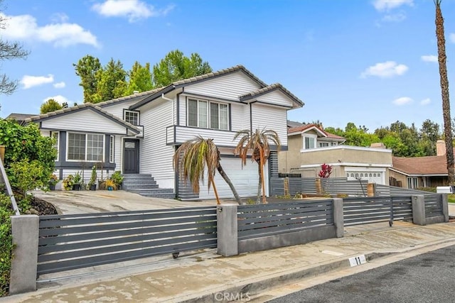 tri-level home featuring a fenced front yard, concrete driveway, a tile roof, and an attached garage