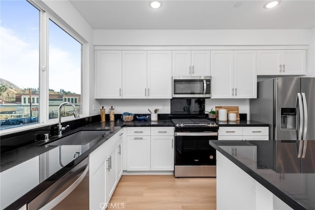 kitchen featuring appliances with stainless steel finishes, light wood-type flooring, sink, dark stone countertops, and white cabinets